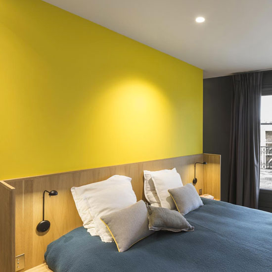 Un jaune lumineux contraste délicatement avec le bleu du linge de lit dans cette chambre parentale