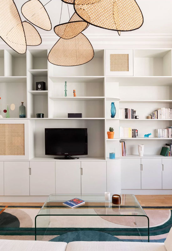 Le cannage contraste avec le blanc du mur de rangement et vases et livres viennent habiller les niches