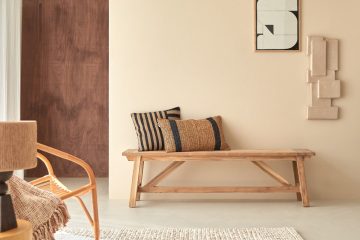 Banc en bois massif dans un séjour beige avec fauteuil en rotin et tapis en laine
