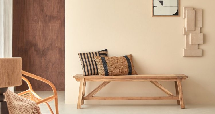 Banc en bois massif dans un séjour beige avec fauteuil en rotin et tapis en laine