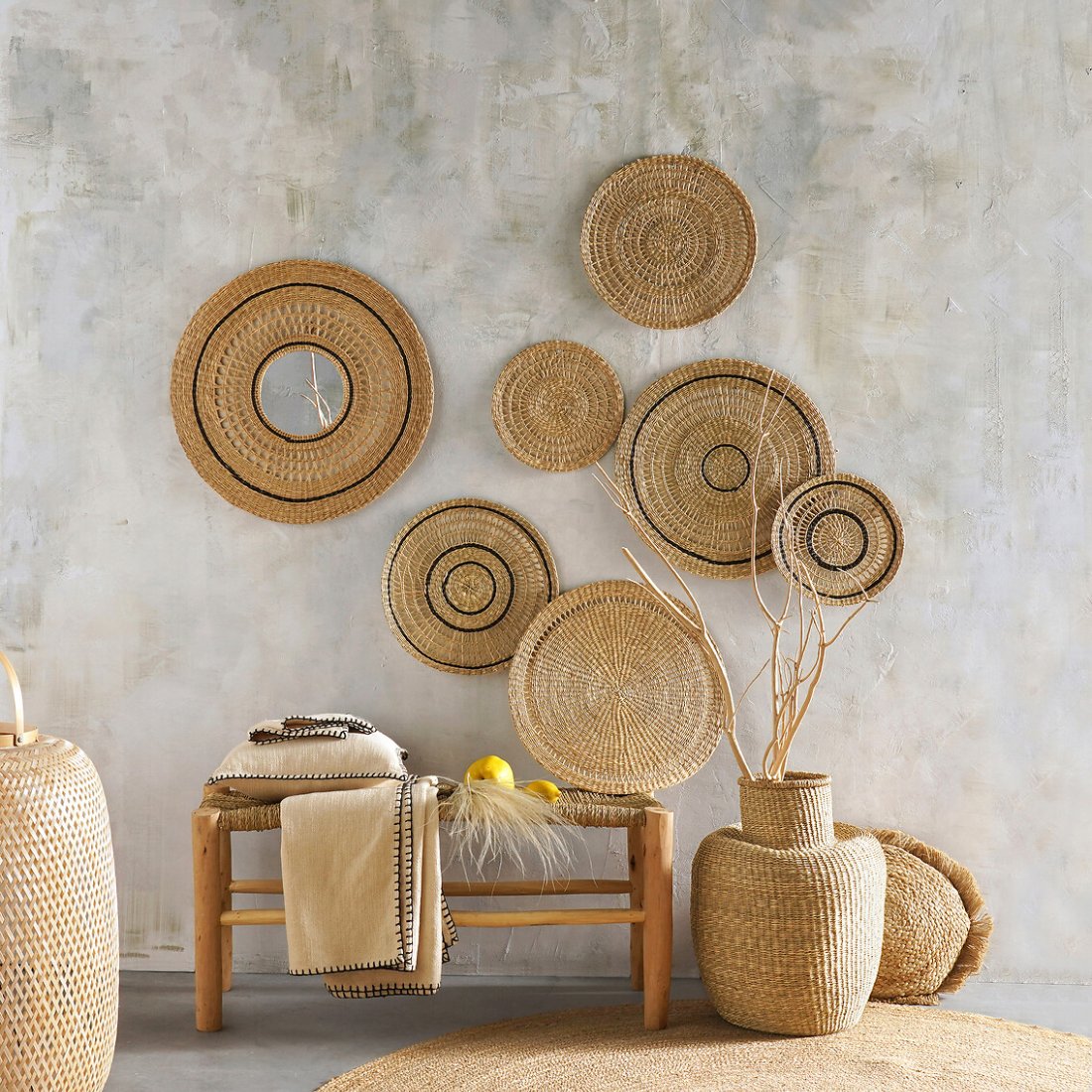 Banc en bois brut Ghada dans un salon devant un mur de plats en fibre tressée