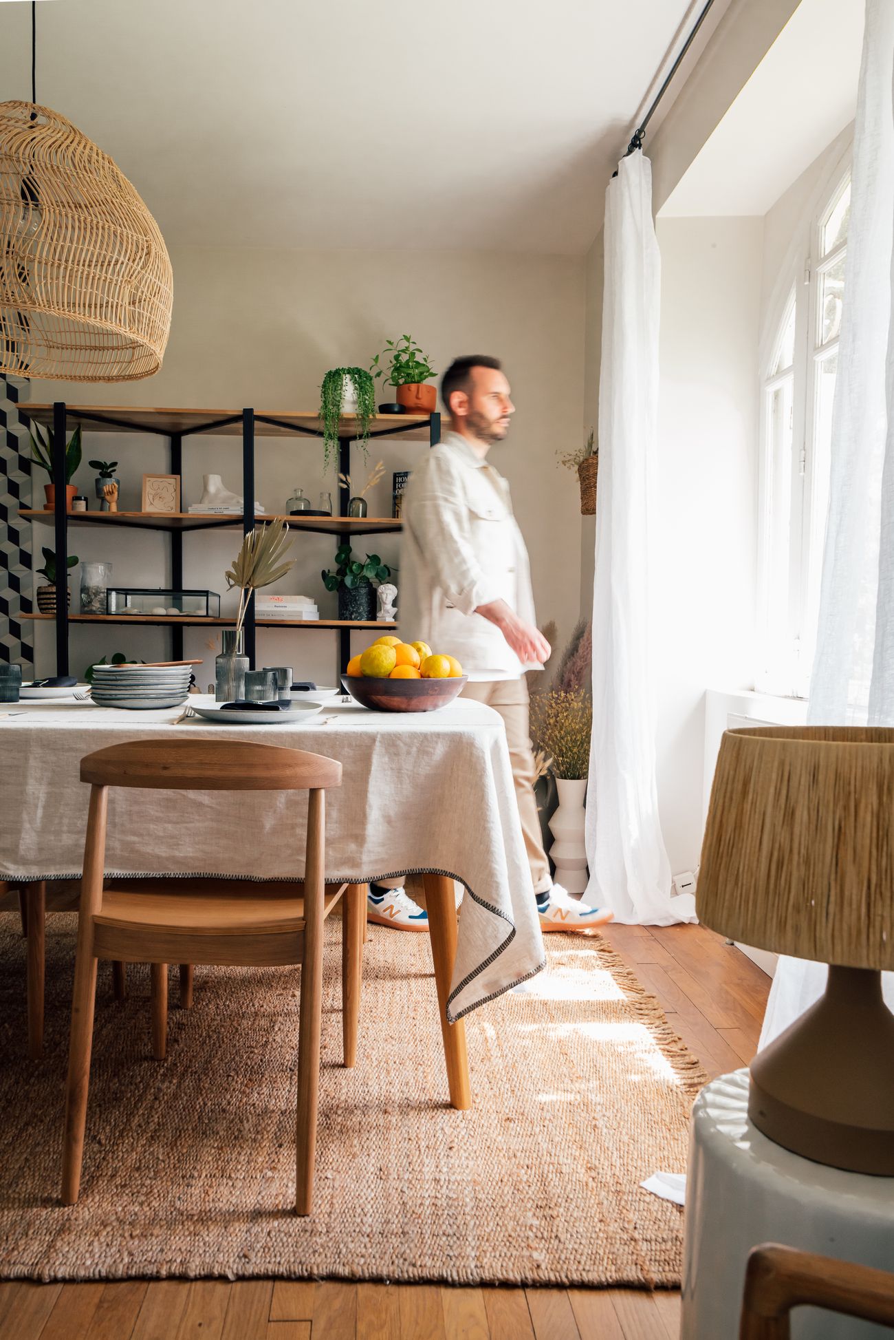 Salle à manger dans l'esprit néo-antique avec suspension en rotin, étagère en métal noir et table dressée pour un brunch