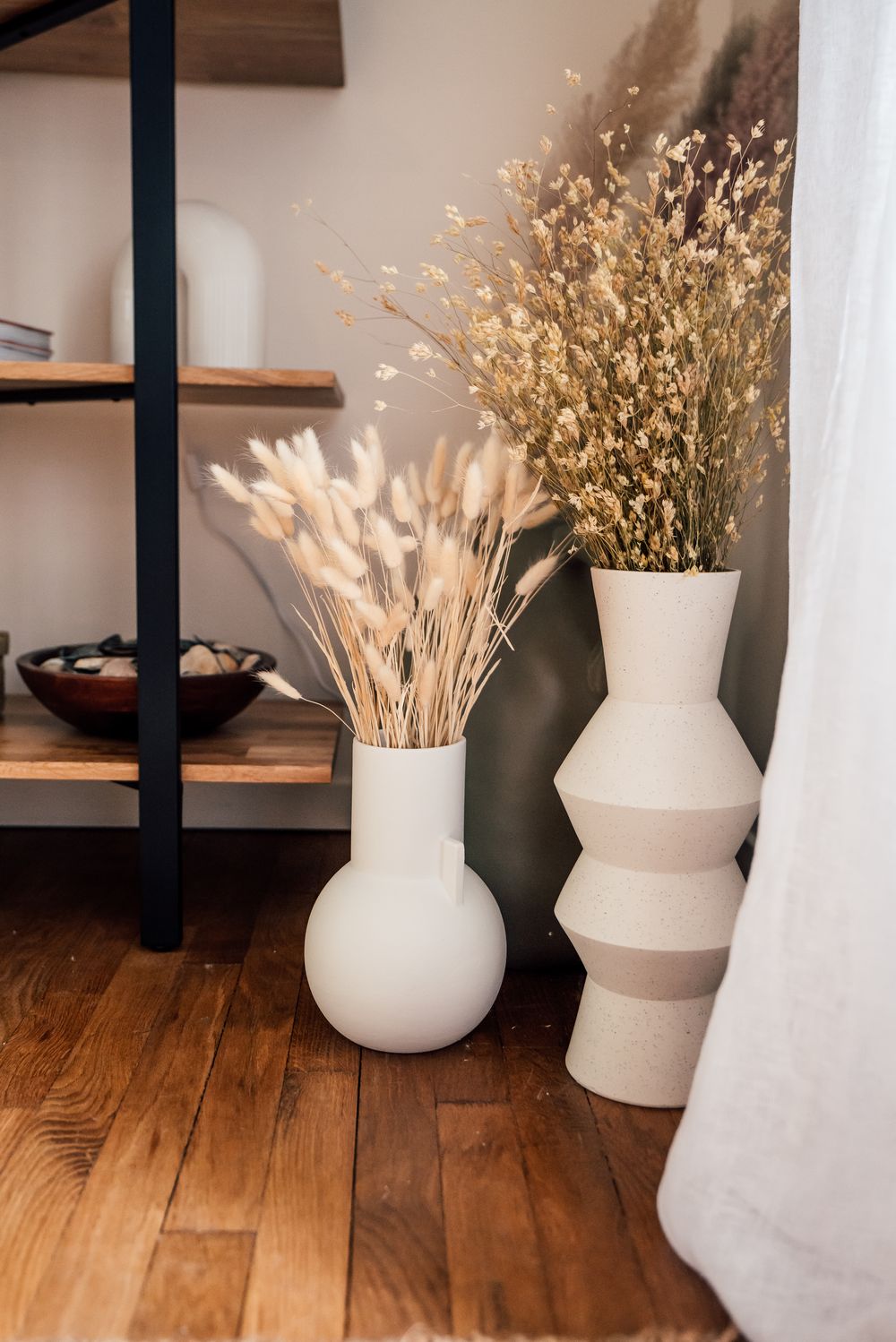 Vases en céramique sculpturale garnis de fleurs séchées, posés au sol dans une pièce aux tons beiges