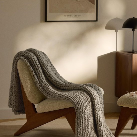 Plaid grosse maille Adyna taupe drapé sur un fauteuil dans un salon