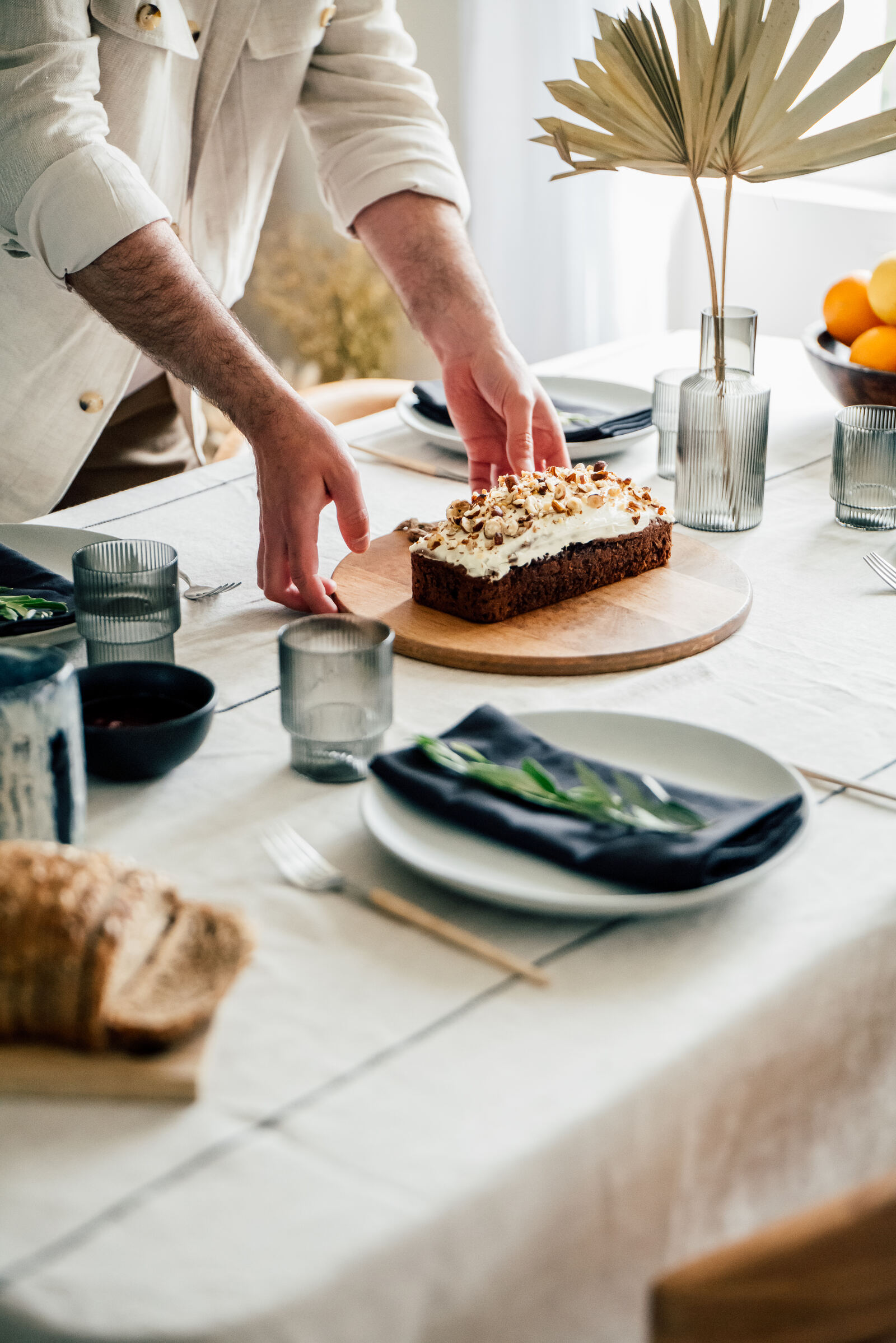 Romain pose un gâteau fait maison sur la table dressée, entourée de vaisselle dépareillée et de linge de table