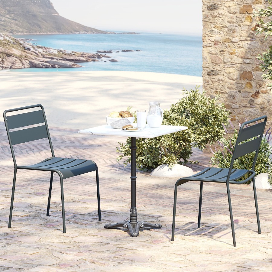 Table de bistrot carree en marbre blanc dressee face a la mer avec deux chaises