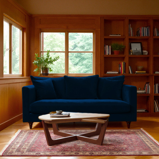 Canapé en velours bleu marine Villabon installé dans un salon cosy avec bibliothèque