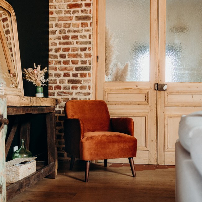 Fauteuil Brooks en velours rouille devant une porte vitree ancienne