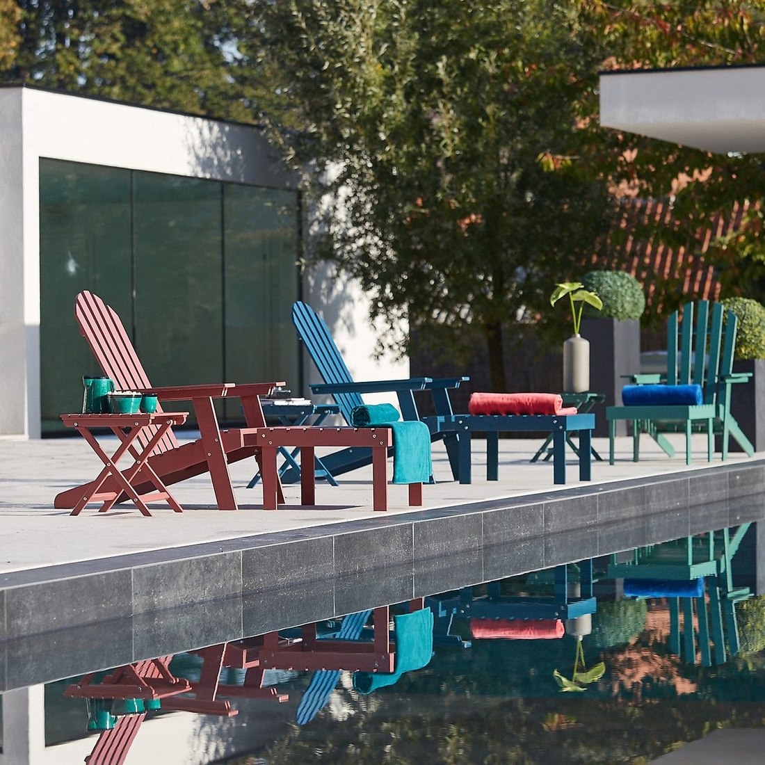 Fauteuils de jardin style Adirondack de coloris variés installés au bord d'une piscine
