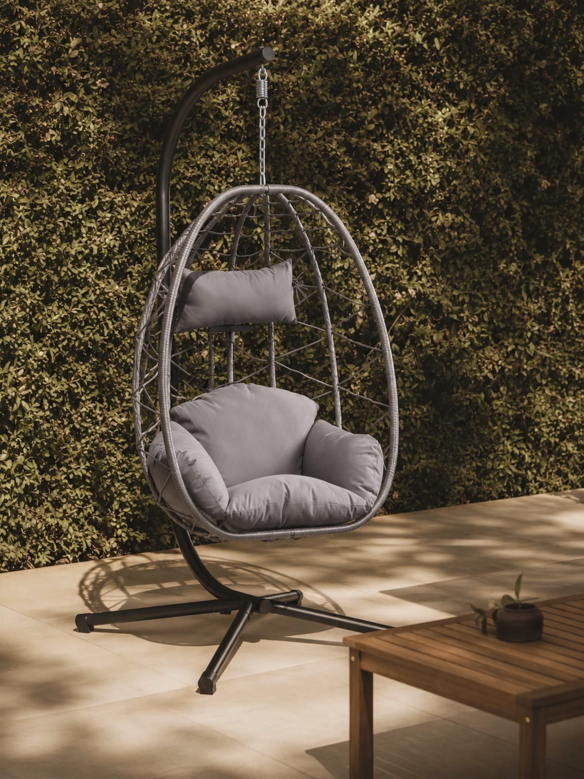 Fauteuil suspendu en rotin et métal noir installé en extérieur sur une terrasse