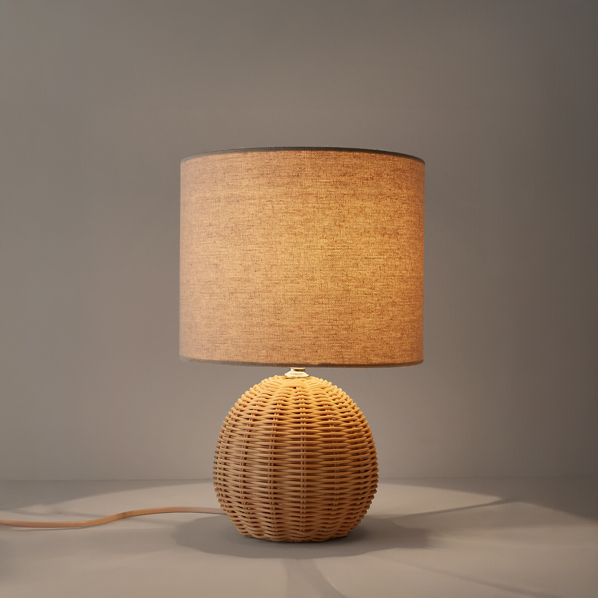 Lampe à poser en rotin et lin HOREA allumée dans une chambre