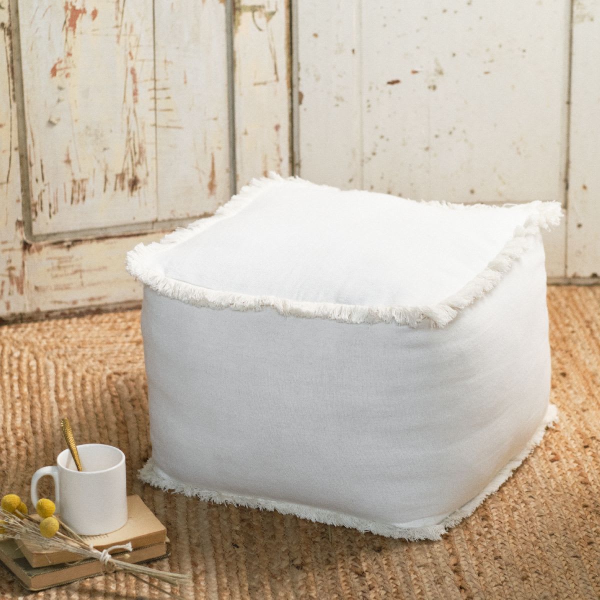 Pouf carré en coton à franges écru Indies de Maisons du Monde posé près d'une table basse