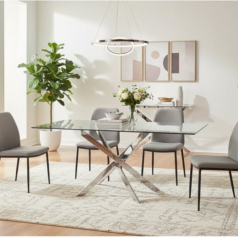 Table en verre transparente Jessica avec pieds chromés croisés et chaises grises dans une salle à manger claire
