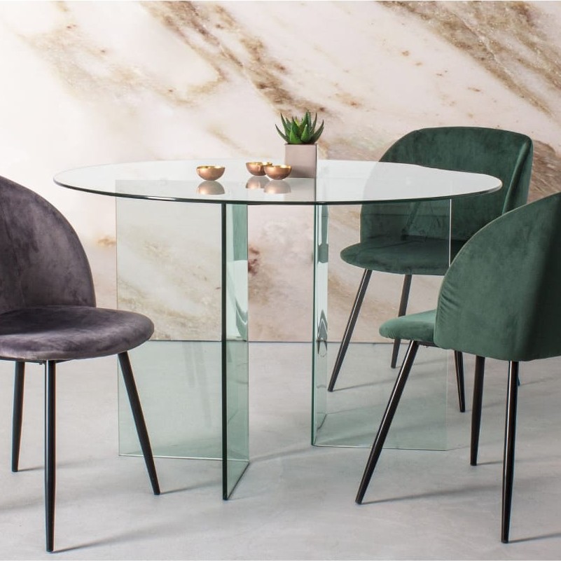 Table à manger ronde en verre transparent Maisons du Monde, entourée de chaises en velours gris et vert