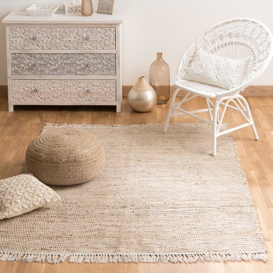 Tapis en jute Lodge Maisons du Monde avec pouf et fauteuil blanc dans un salon lumineux